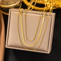 Close-up of golden layered snake chain and ring necklaces on a beige jewelry box - Triple Layer Mixed