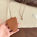 Macro shot of brown faux leather crescent pendant with fine stitching on a woven mat - Red-Brown Glasses Clip