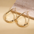 Macro detail showing high-gloss gold plated twisted teardrop earrings on a stone stand - Gold