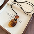 Gros plan du pendentif goutte en acrylique ambre sur cordon noir dans une boîte cadeau - Brun Foncé (Ambre)