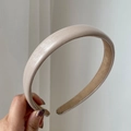Minimalist beige leather headband with soft fabric lining held against a neutral wall - Off White