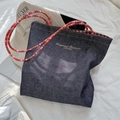 Detailed view of a retro denim tote bag featuring colorful braided handles and gold embroidery - Red-Orange Strap