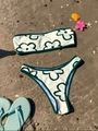 Flat lay of floral bandeau bikini with green trim on sandy beach with summer props - Off White