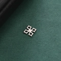 Macro shot of silver stainless steel geometric hollow charm on a green textured background - Hollow Cross Flower Style / Silver