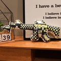 Yellow pixelated assault rifle plush pillow in a cozy home setting on a wooden table - Yellow Machine Gun Style