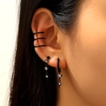 Macro detail of black cross and star earrings set with purple zirconias on ear - Gothic Set with Moon Rhinestone Drop and Chain Stud (9650)