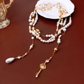 Detail of multilayer pearl necklace with gold key pendant on a white ceramic plate - Necklace - Gold - White