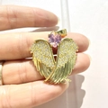 Detail view of golden angel wing pendant with clear crystals and a pink heart gem - Gold-Pink