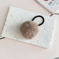 Macro detail of fluffy coffee brown faux fur pom pom hair tie on white marble surface - Brown