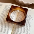 Macro shot of an amber acrylic ring placed on a book page with vintage warm tones - Retro Thick Square-Round Style / Coffee Caramel Amber