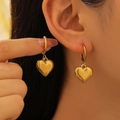 Close-up of polished gold heart dangle earrings on model highlighting the elegant metal shine - Stainless Steel / 3D Heart Pendant - Gold