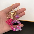 Detail of letter Q resin keychain with pink sequins, pompom and golden accessories - Small Ball Tassel Clasp / Letter Q