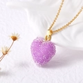 Gros plan sur le pendentif cœur lavande étincelant avec chaîne dorée sur fond en relief - Violet