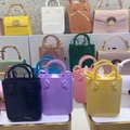 Close-up of stylish PVC jelly handbags in multiple colors with bamboo handles on a shelf - Coffee