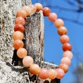 Macro view of sunstone bead bracelet on dry wood against a clear blue sky background - Pink Aventurine