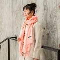 Pink cashmere scarf with fringe details worn by a model against a grey wall - Snow Bud