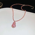Makroaufnahme einer 18K vergoldeten rosa Kristallkette mit Hulu-Anhänger auf weißem Teller - Rosa Strass Gourd Halskette