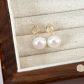 Close-up of minimalist white freshwater pearl earrings with gold pins on a jewelry box - 10mm Pink Light Pearl