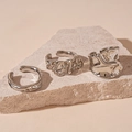 Detalle macro de tres anillos de plata de metal líquido irregular sobre piedra natural - Juego de Anillos Abiertos Plisados / Plateado