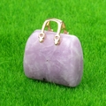Miniature pink quartz handbag pendant with a gold metal handle on green grass - Lilac Stone