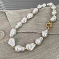 Detailed macro view of baroque pearl necklace with golden OT clasp on soft grey fabric - Style 1