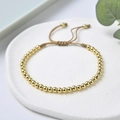 Detail eines verstellbaren geflochtenen Armbands mit polierten Goldperlen auf Stein - Gold Perlen Seil