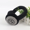 Macro view of plush children's winter earmuffs with a black smiley face pattern detail - Black