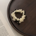 Dettaglio di scrunchie plissettato crema con piccoli fiocchi neri su vassoio in legno - Scrunchie a pieghe bianco con fiocchi neri