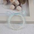Close-up of children's white faux pearl bracelet with a blue satin ribbon bow detail - 6MM Cream White Pearl With Blue Ribbon Bracelet
