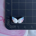 Macro shot of tiny resin wing accessory with pastel gradient tips on a measurement scale - Colored Double Wings