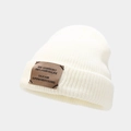 Close-up of white knit beanie featuring thick texture and a brown decorative patch - White