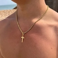 Collar para hombre de cadena salomónica dorada con cruz lucido por un modelo en la playa - Dorado