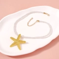 Detailed view of a gold starfish pendant on a white braided cord for beach vacations - Necklace D-Braided Cord Starfish