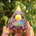 Pyramide d'orgonite avec améthyste, feuilles d'or et symbole Om tenue devant la nature - Style 30