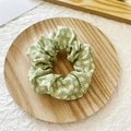 Daisy floral print scrunchie in light green fabric displayed on a wooden tray - Green Floral