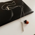 Detail shot of a silver metal cylinder and dark wooden acorn pendant on black leather - Silver-Brown
