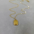 Close-up of golden square pendant engraved with Where is love on a textured grey background - Chocolate Necklace