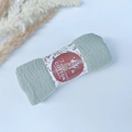 Pleated light green cotton scarf rolled with floral label on a soft blue surface - Style #25
