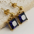 Macro shot of gold drop earrings with square-cut dark blue zircon on textured stone - Blue