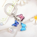 Detail of alloy butterfly keychain with colorful drip oil pendants on a floral background - Style 11 M749 (Pink/Purple/Blue Butterfly)