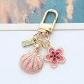Close-up of golden keychain with pink enamel shell and flower charms on white surface - Pink Shell