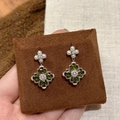 Macro shot of green clover flower earrings with pearls and crystals on a brown cushion - Four-leaf Clover Style / Silver Earring Post-Green