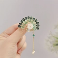 Macro shot of peacock brooch featuring green enamel feathers and elegant pearl tassels - Peacock