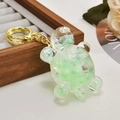 Creative light green liquid glitter turtle keychain with golden ring on wooden tray - Nocturnal Fruit Green