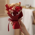 Close-up of mini red soap roses and baby's breath wrapped in red and gold paper - Red