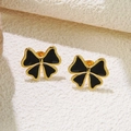 Close-up of gold-rimmed black bow earrings on white textured stone background - Black