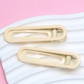 Detail view of two cream beige glossy metal hair clips on a wavy pink surface - Off White