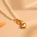 Dettaglio di collana di perle con ciondolo a cuore dorato e chiusura a T su conchiglia - Oro