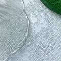 Nahaufnahme schillernder Glas-Bubble-Perlen für Nailart auf weißem Textilgewebe - Eisiges Weiß
