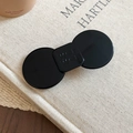 Detail view of a black resin hair clip with engraved letters on a textured book surface - Geometric Bow Style / Black / Large
